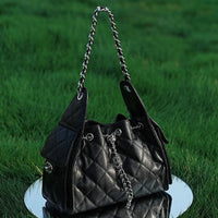 Quilted black leather handbag with chain strap on grass and mirror background