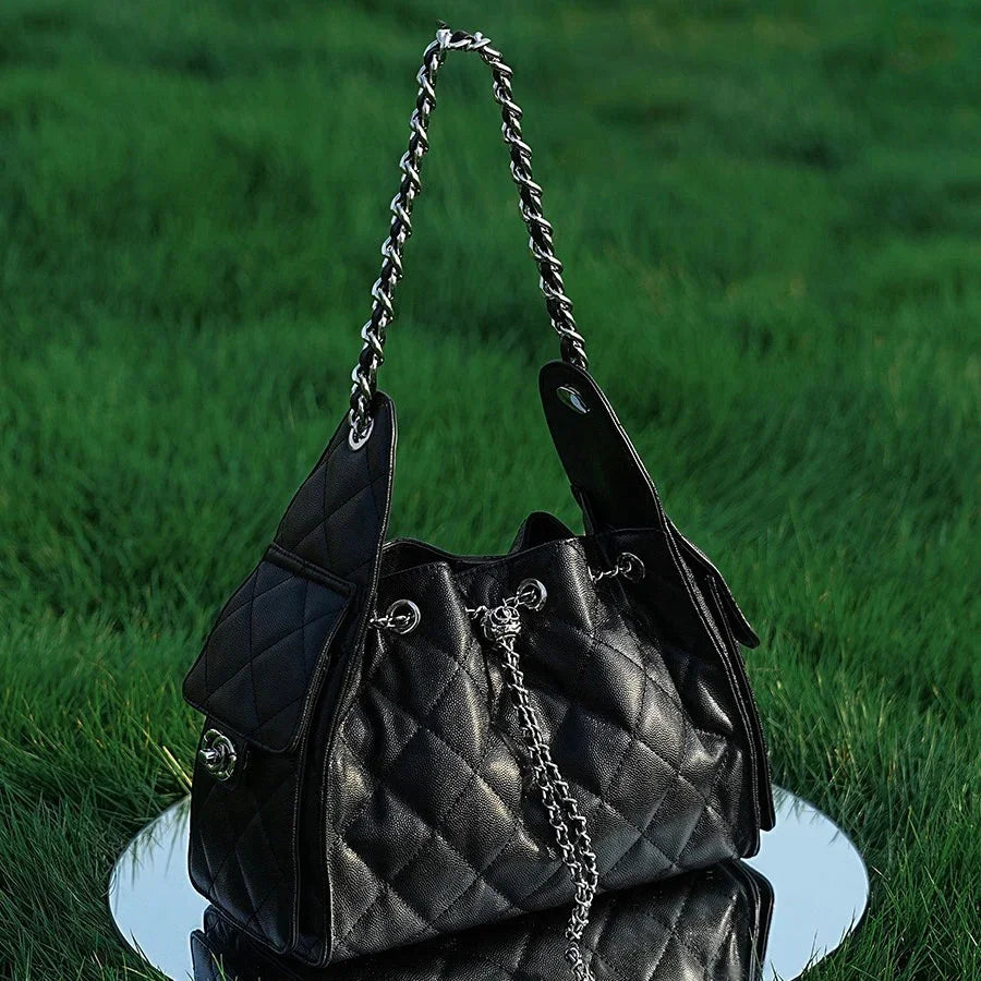 Quilted black leather handbag with chain strap on grass and mirror background