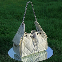 Quilted white handbag with chain strap on mirror in grass, stylish women's accessory