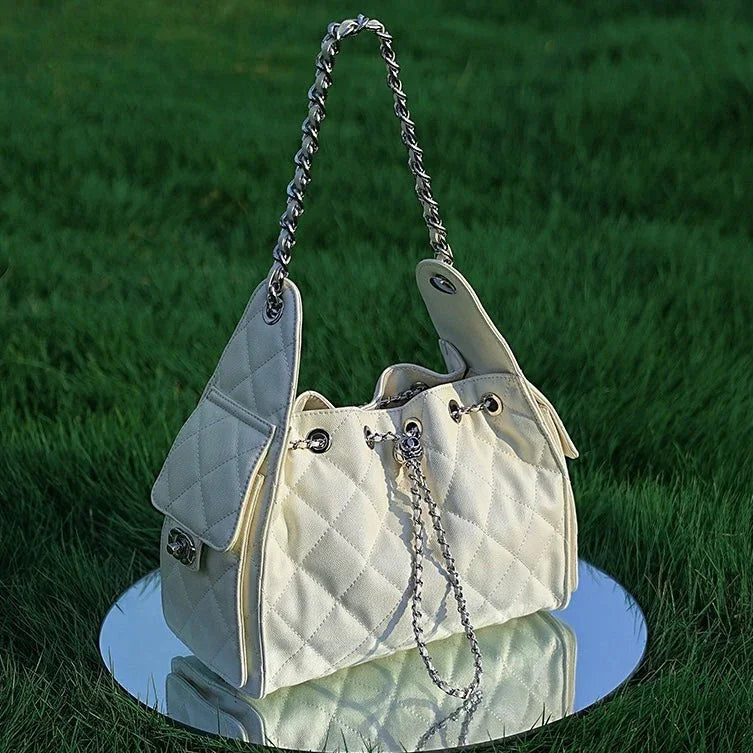 Quilted white handbag with chain strap on mirror in grass, stylish women's accessory