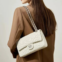Woman in brown blazer with white quilted shoulder bag and chain strap