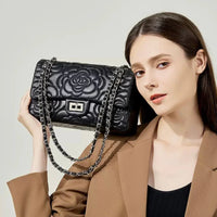 Woman holding a black quilted floral leather handbag with chain strap