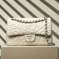 Quilted white leather handbag with chain strap and floral pattern on beige pedestal