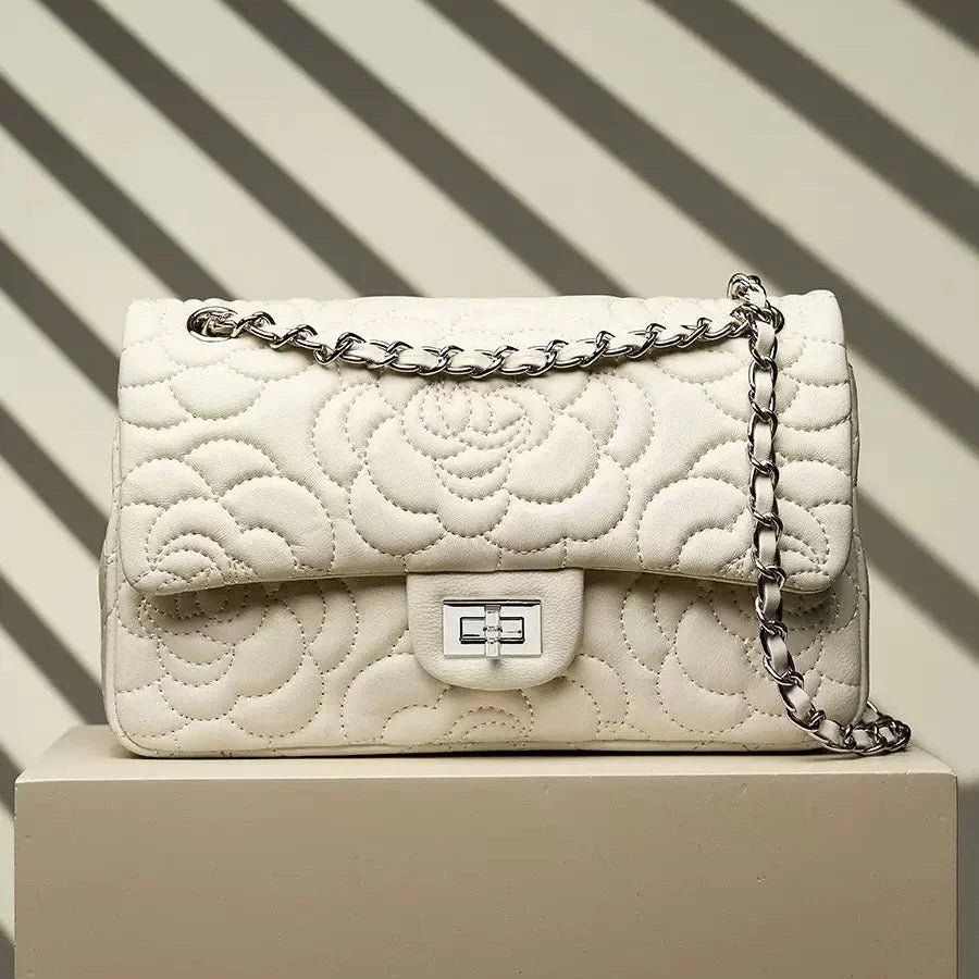 Quilted white leather handbag with chain strap and floral pattern on beige pedestal