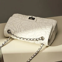 White quilted floral handbag with silver chain strap on cream table
