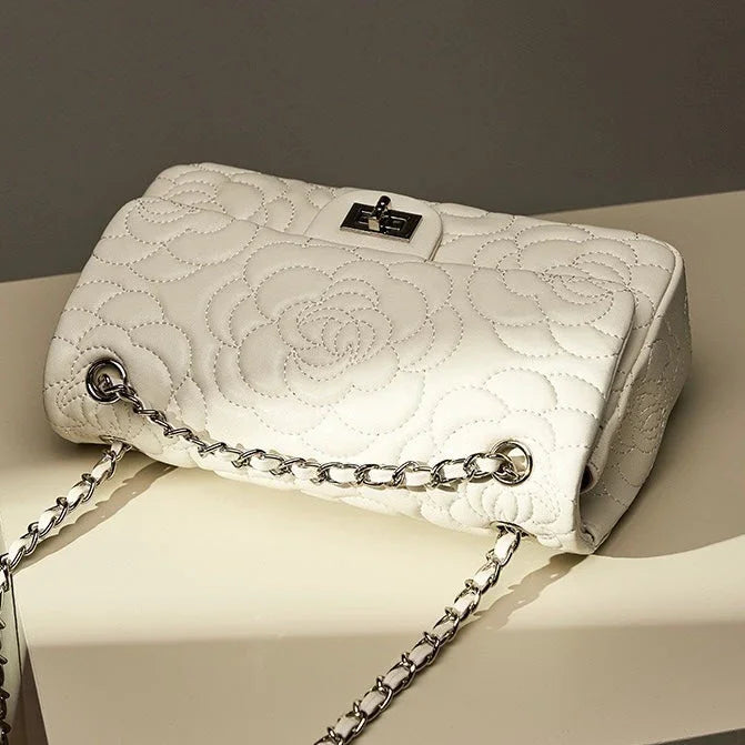 White quilted floral handbag with silver chain strap on cream table