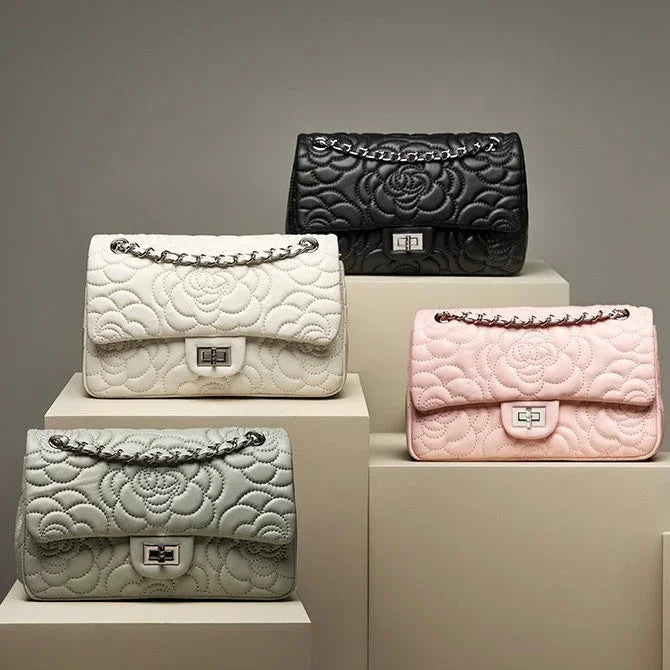 Four quilted floral leather handbags in black, white, pink, and gray on display pedestals