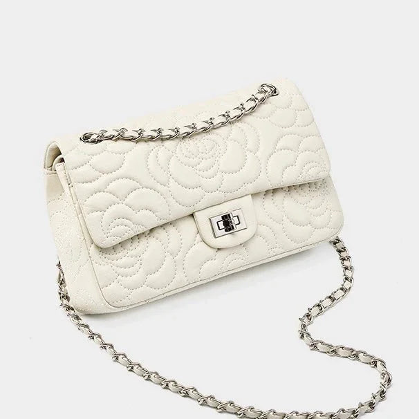 White quilted leather shoulder bag with floral pattern and silver chain strap on white background