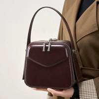 Woman holding a brown leather box handbag with silver zippers and top handle