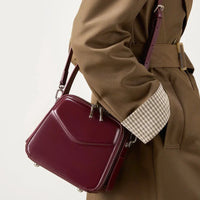 Woman wearing tan coat with maroon square crossbody bag, stylish fashion accessory