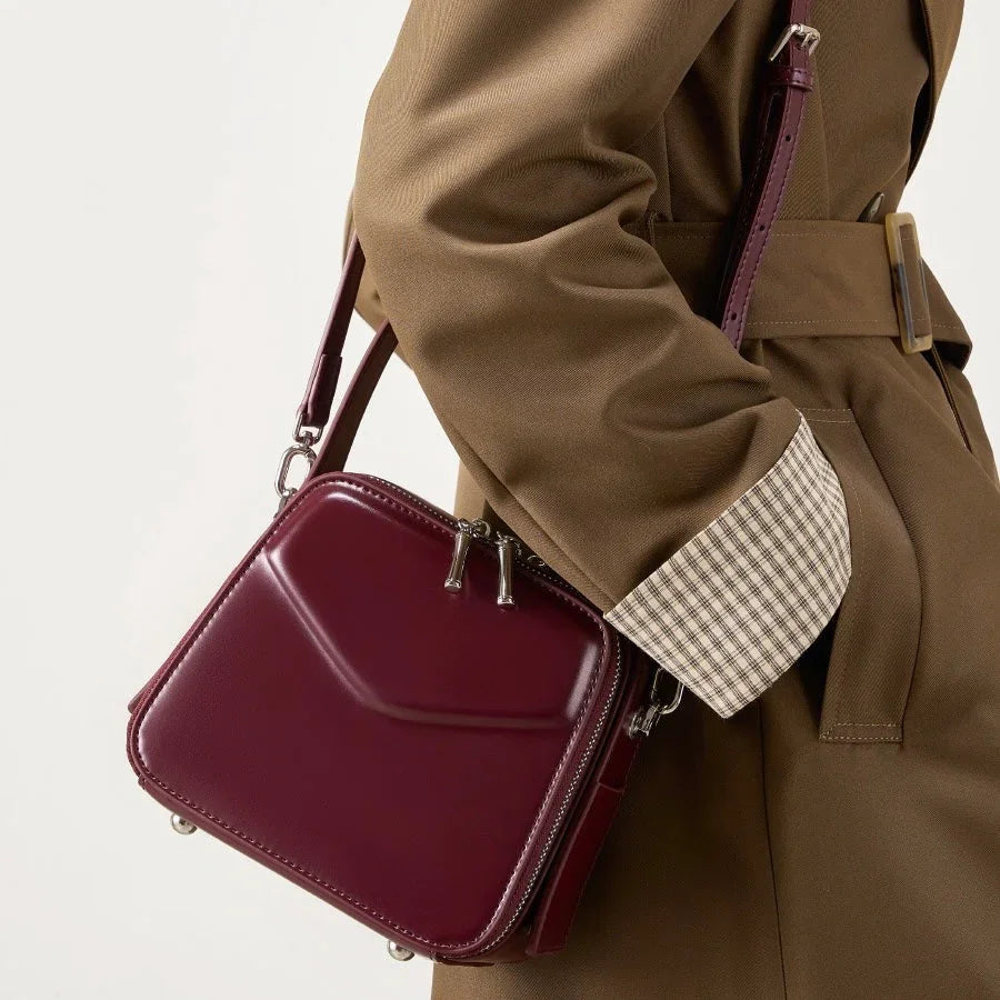 Woman wearing tan coat with maroon square crossbody bag, stylish fashion accessory
