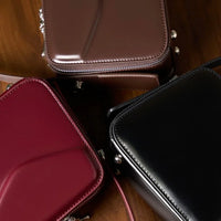 Three square leather crossbody bags in black, burgundy, and brown on wooden surface