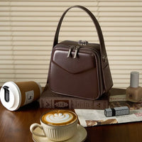 Brown leather handbag on books with coffee, lipstick, nail polish, and blinds background