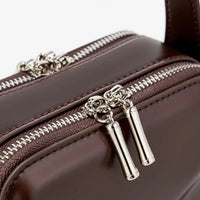 Close-up of brown leather bag with silver zippers and metallic pull tabs