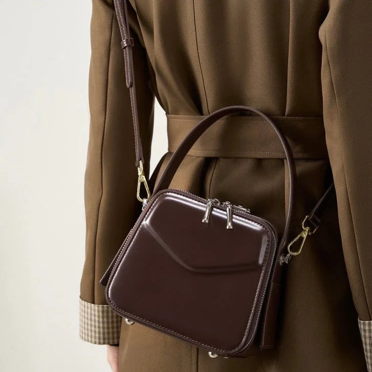 Glossy brown leather crossbody square bag on person in brown coat, fashion accessory