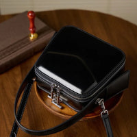 Glossy black square crossbody bag with zipper and silver hardware on wooden table
