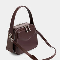 Brown leather square crossbody bag with top handle and silver zippers on white background