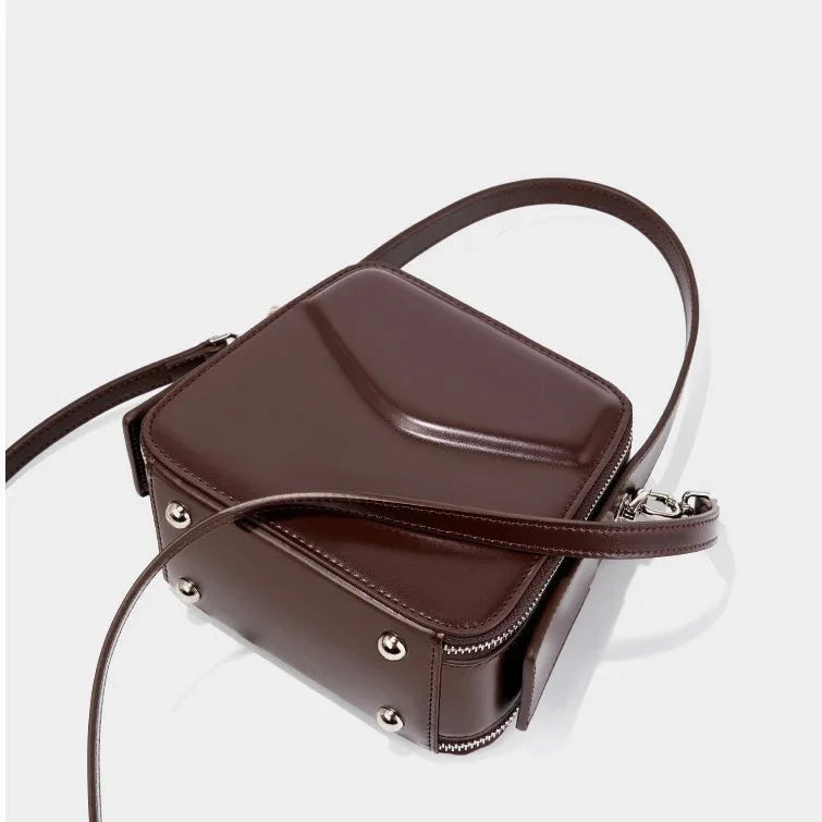 Brown box-shaped leather crossbody bag with metallic studs and a smooth surface