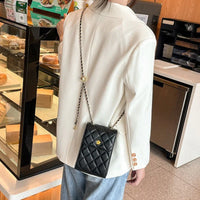 Woman in white blazer with black quilted crossbody purse near bakery display case