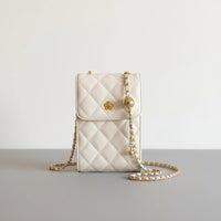 Cream quilted crossbody bag with gold chain strap and flower detail held by hand