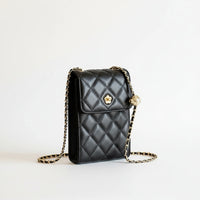 Quilted black leather crossbody bag with gold chain and flower clasp, held by a hand