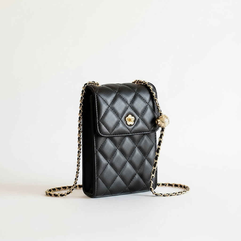 Quilted black leather crossbody bag with gold chain and flower clasp, held by a hand