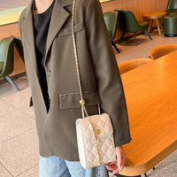 Woman in brown blazer with quilted beige crossbody bag at modern cafe table