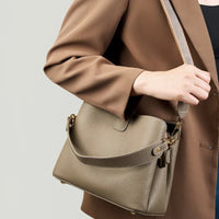 Woman in brown blazer carrying taupe leather shoulder bag with gold hardware