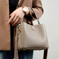 Woman in brown blazer holding taupe leather handbag with gold hardware