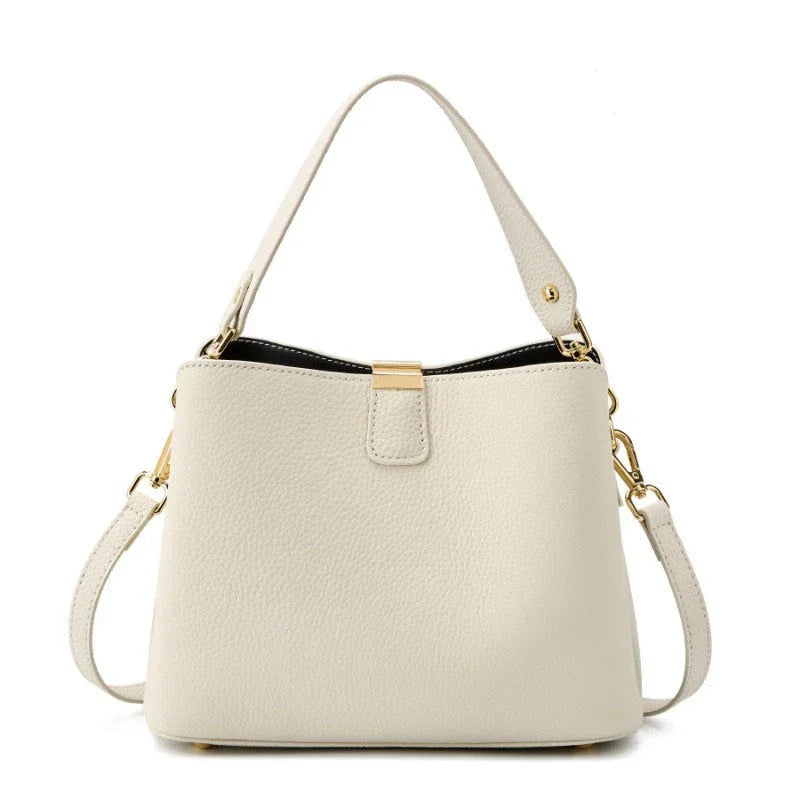 Beige leather handbag with gold hardware and detachable shoulder strap on white background