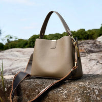 Taupe leather handbag with gold hardware on a rock outdoors, luxury fashion accessory