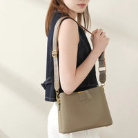 Woman wearing a taupe leather shoulder bag with gold hardware and wide strap