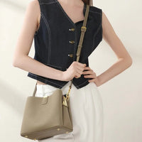 Woman wearing a navy vest and white pants with a taupe leather bucket bag