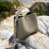 Taupe leather handbag with gold hardware on rocks outdoors