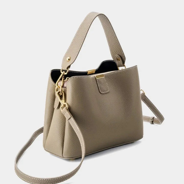 Taupe leather handbag with gold hardware and adjustable shoulder strap on white background