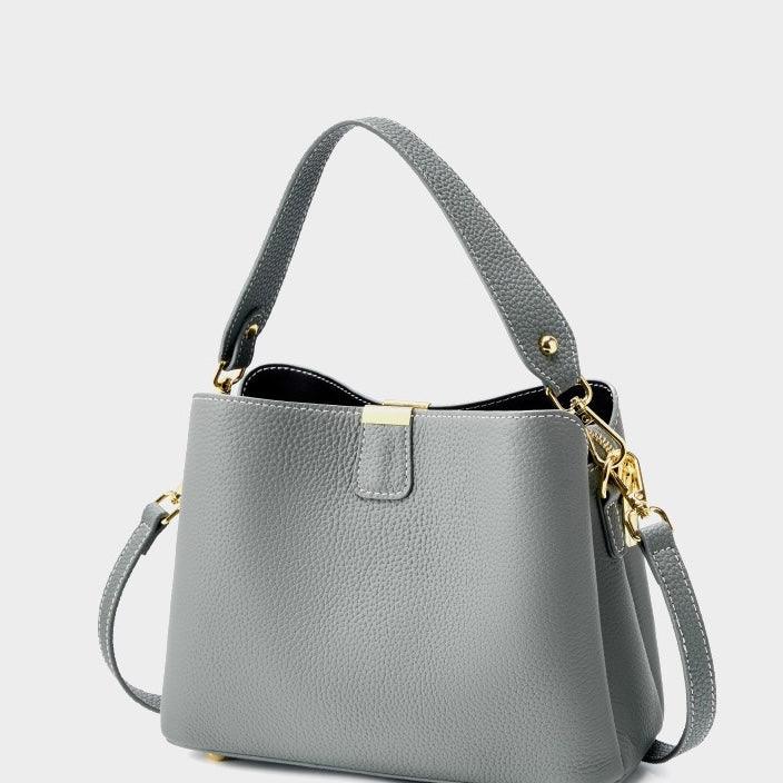 Gray leather handbag with gold hardware and shoulder strap on a white background