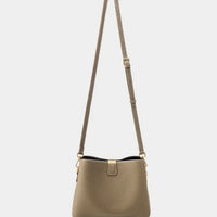 Taupe leather crossbody bag with adjustable strap and gold hardware on white background