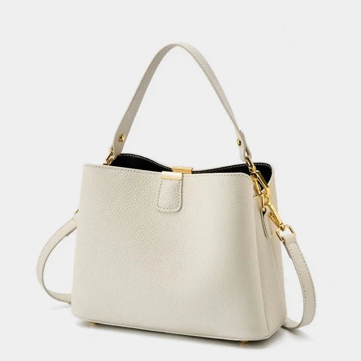 Beige leather handbag with gold hardware and detachable shoulder strap on white background