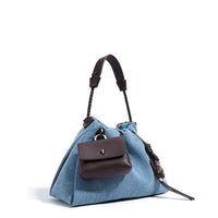 Blue denim handbag with brown leather handle and front pocket on white background