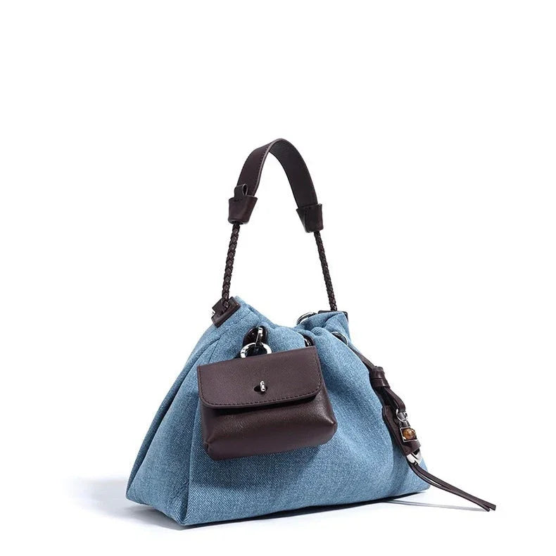 Blue denim handbag with brown leather handle and front pocket on white background