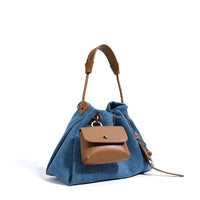 Blue denim handbag with tan leather handles and front brown leather pouch, studio background