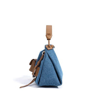 Side view of blue denim handbag with brown leather strap on white background