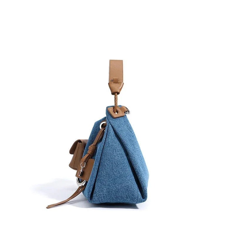 Side view of blue denim handbag with brown leather strap on white background