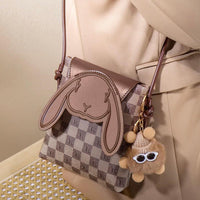 Patterned crossbody bag with bunny face flap and fluffy bear keychain, beige outfit