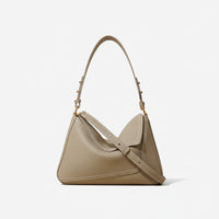 Taupe leather shoulder bag with gold hardware and top handle on neutral background