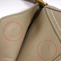 Close-up of textured taupe leather handbag with red circles and white stitching details