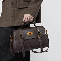 Woman holding a dark brown leather satchel handbag with gold hardware