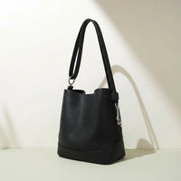 Black leather bucket bag with shoulder strap on light surface, minimalist background