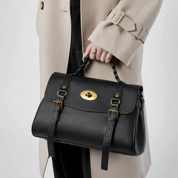 Woman in beige coat holding black leather handbag with gold buckle details