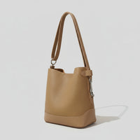 Tan leather bucket bag with shoulder strap on light background, minimalist fashion accessory